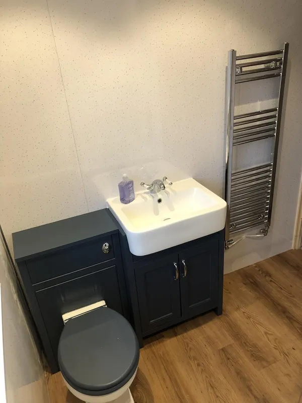 A navy vanity unit and toilet with a chrome towel rail on a wood-effect floor