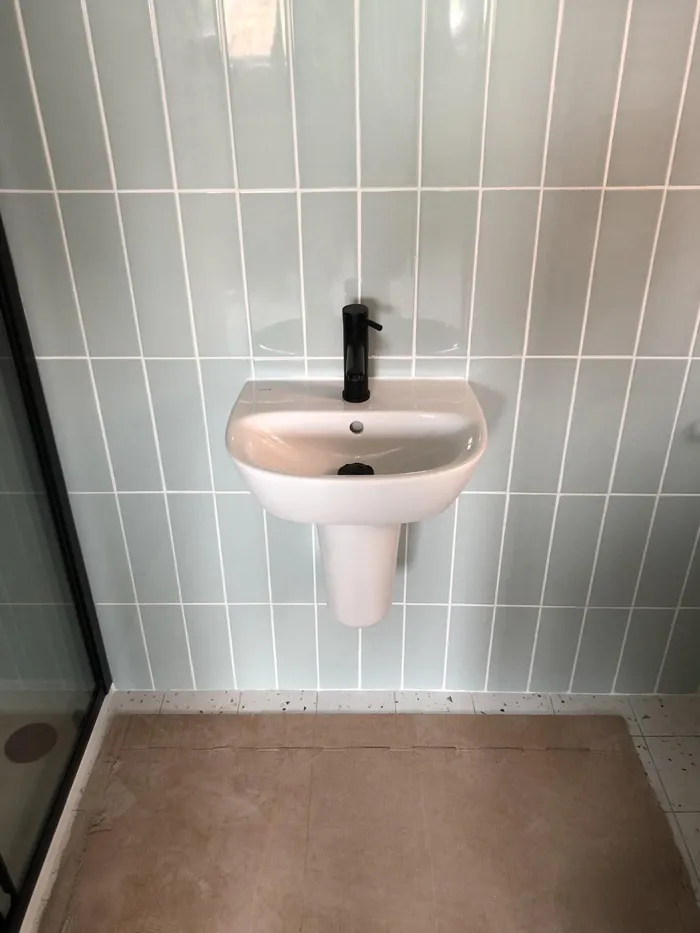 A shower room with sage green vertical tiles and a wall-hung basin