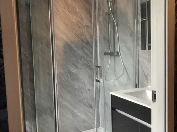A walk-in shower enclosure with grey marble-effect wall panels